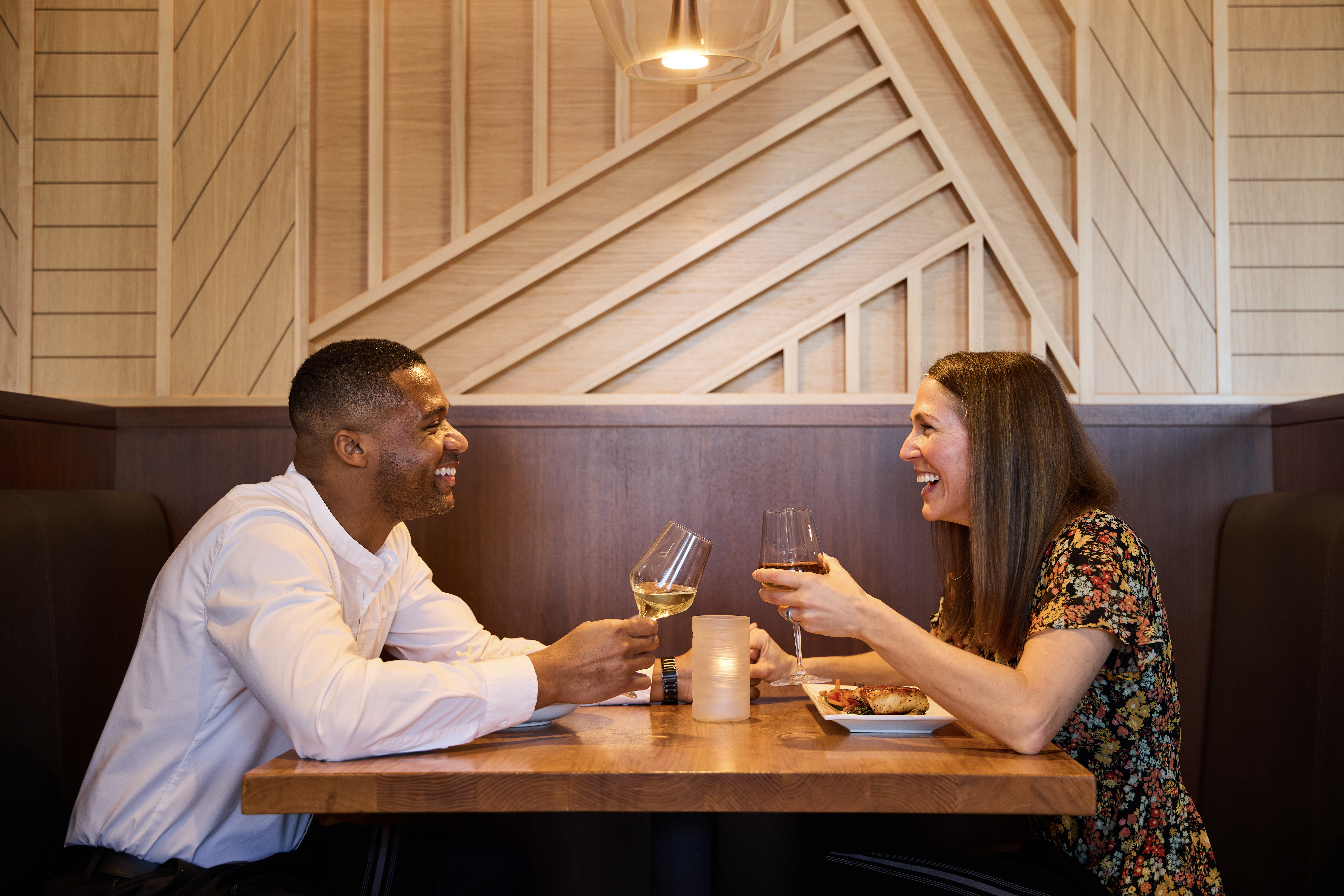 man and woman sitting across from eachother in a restaurant booth holding wine glasses